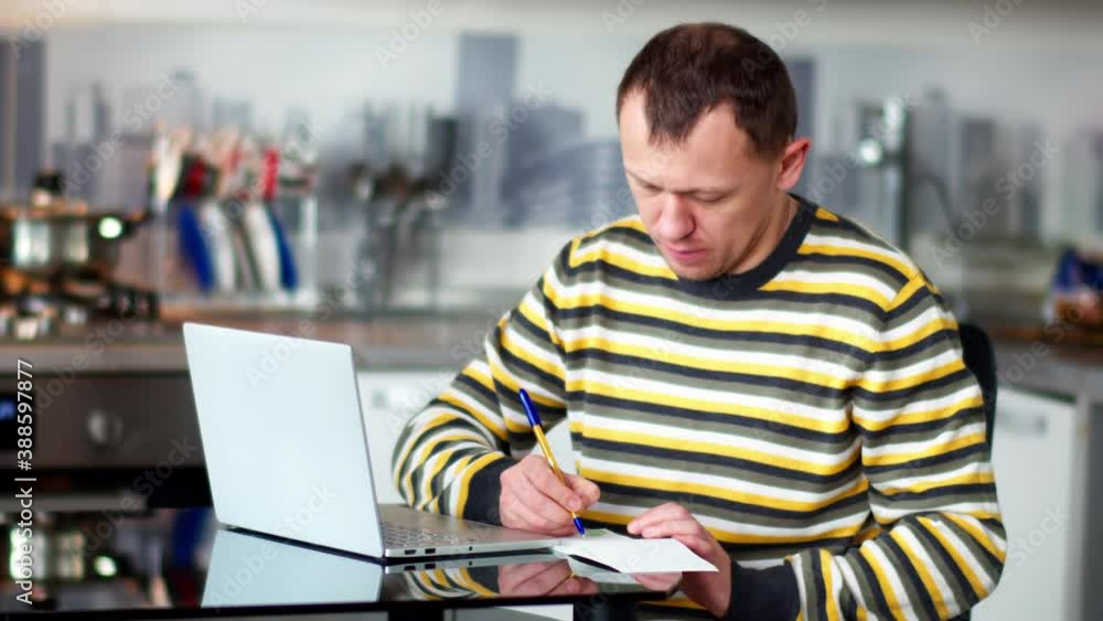 Young man working at home using laptop, making notes in notebook Young man working at home using laptop, making notes in notebook