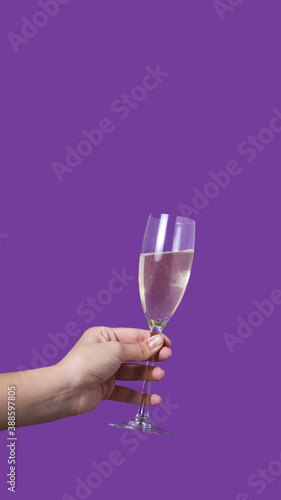 A glass of champagne in the woman's hand purple background