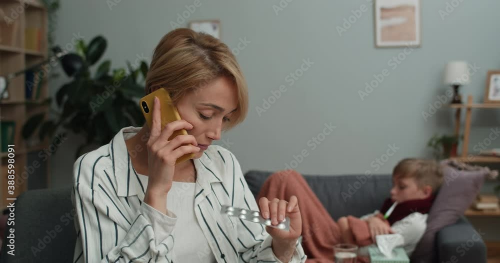 Loving mother calling and talking on mobilephone with doctor while holding pills blister. Ill teen child lying on sofa with thermometer why measuring temperature. Concept of healthcare Loving mother calling and talking on mobilephone with doctor while holding pills blister. Ill teen child lying on sofa with thermometer why measuring temperature. Concept of healthcare