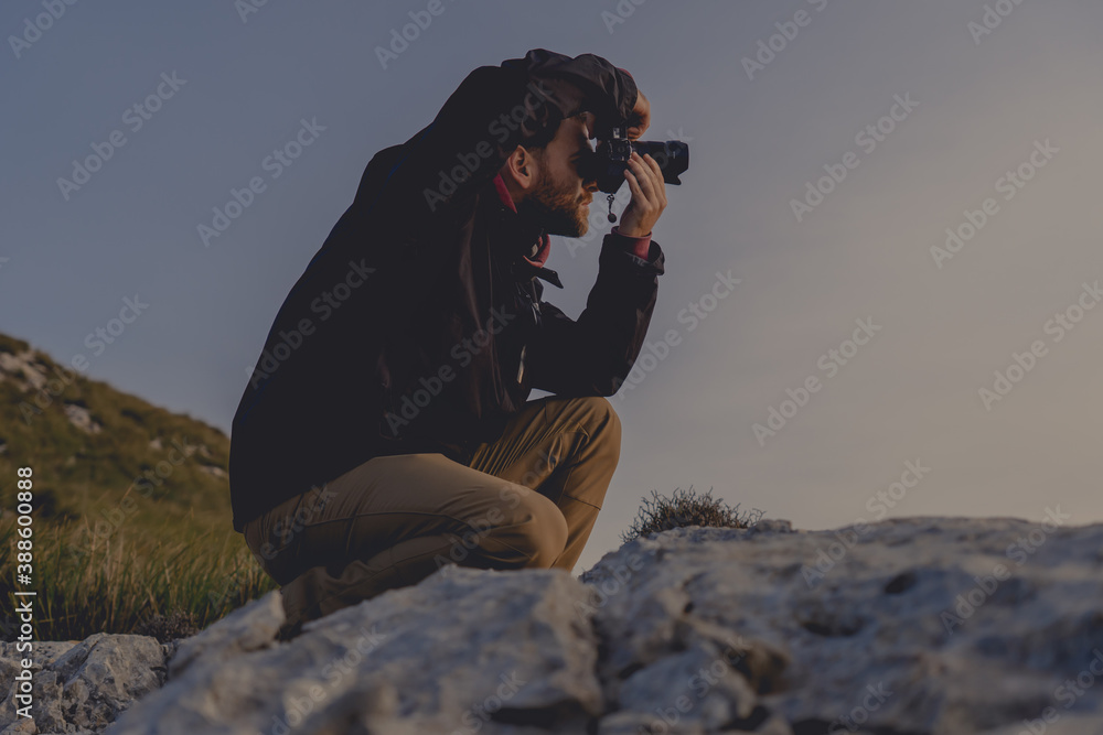 Close-up of young hiker man in profile taking photograph in the sunrise sun, image with soft tones and cold lights