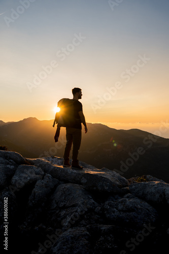 Vertical image of hiker at the top of a mountain enjoying the beautiful golden hour sunset with intense color and blue sky fused with yellow, carrying a large backpack