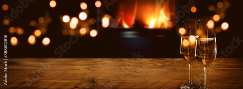 Champagne on rustic wood in front of a log fire with golden bokeh lights. Horizontal background for celebrations and cozy evenings with space for your text and decorations. photo