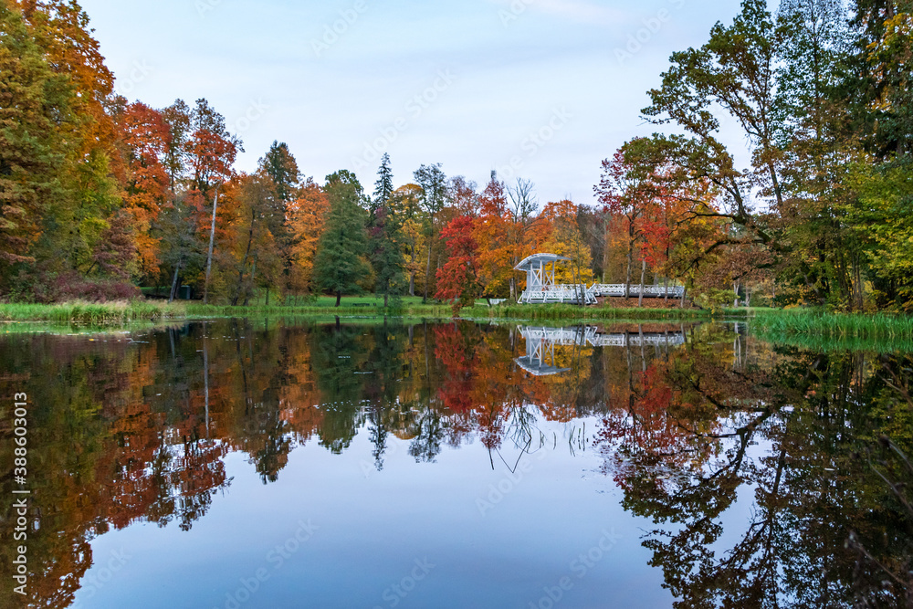 Autumn landscape with reflection in the park canal with a white stage on the island