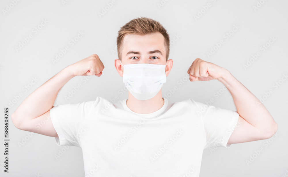 Portrait of a handsome American man wearing medical protective mask standing with a raised arm shows strong biceps. Isolated background. Portrait of a handsome American man wearing medical protective mask standing with a raised arm shows strong biceps. Isolated background.