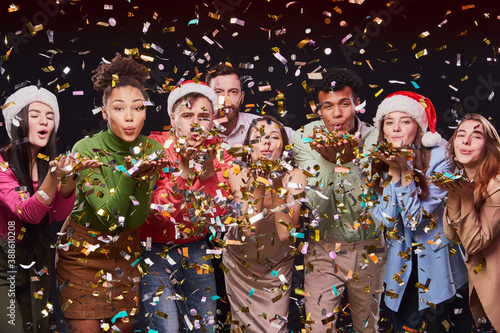 Celebrating New Year 2021 together. Group of young multiracial happy people blowing colorful confetti