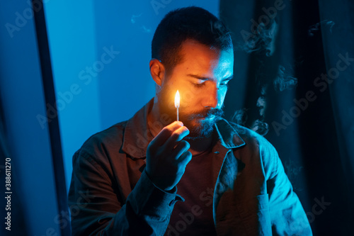Portrait of a bearded man in a dark room lighting a matchstick. Spooky concept