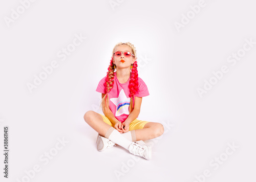 a cute girl in bright colorful clothes and with colored braids shows gelatinous gummies