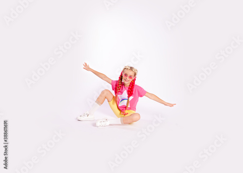 cute girl in bright colorful clothes and with colored braids and bright sunglasses shows exercises on a white background
