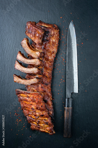Traditional barbecue pork spare ribs spicy marinaded with chili offered with a Japanese knife as top view on a black board