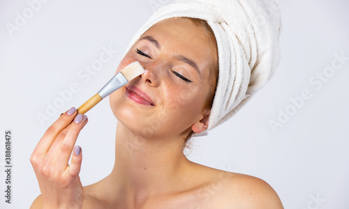 A girl with a towel on her head and hangs on her face  applies a gel mask with a brush. Fashionable female model with beautiful appearance. Photo on white background