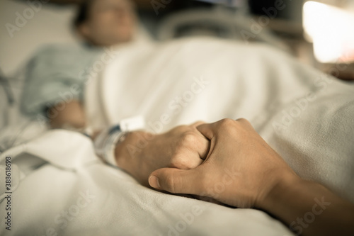 Fotografia Person holding sick woman's hand lying in hospital bed.