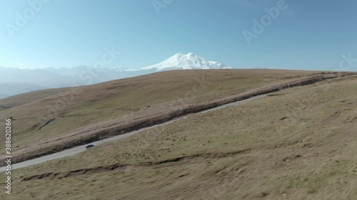 Travel car driving in highland road on snowy mountain peak landscape. SUV car moving on highway to Dzhily Su in Kabardino-Balkaria. Aerial side shooting from flying drone. photo