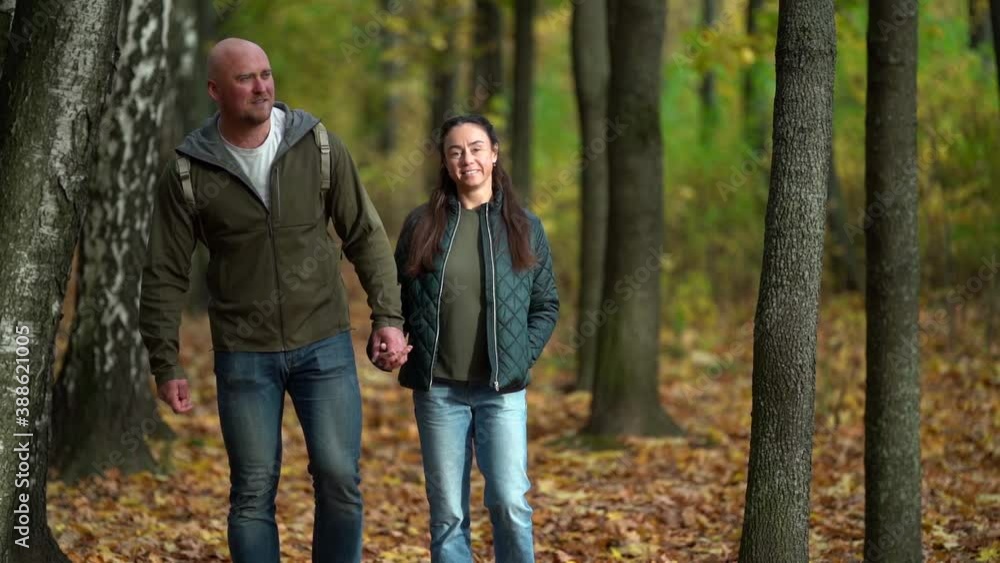 happy married couple of middle-aged man and woman holding hands are walking in autumn forest at daytime happy married couple of middle-aged man and woman holding hands are walking in autumn forest at daytime