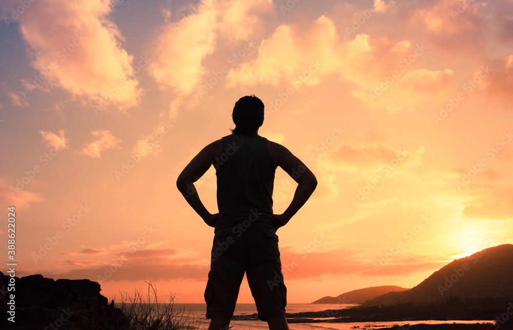 silhouette of young thoughtful man standing watching the sunset on a mountain top