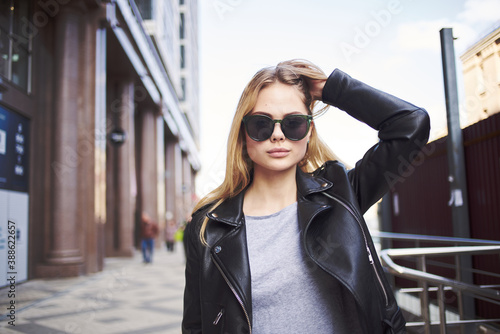 Happy woman model in a leather jacket walks down the street