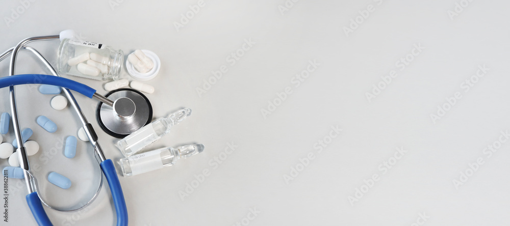 Fototapeta premium Medical stethoscope on a gray background with pills. Coronavirus pandemic new normal concept top view banner