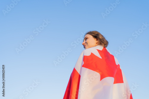 A person with a flag on shoulders looks proudly into the distance. Clear skies in the background. Canadian flag