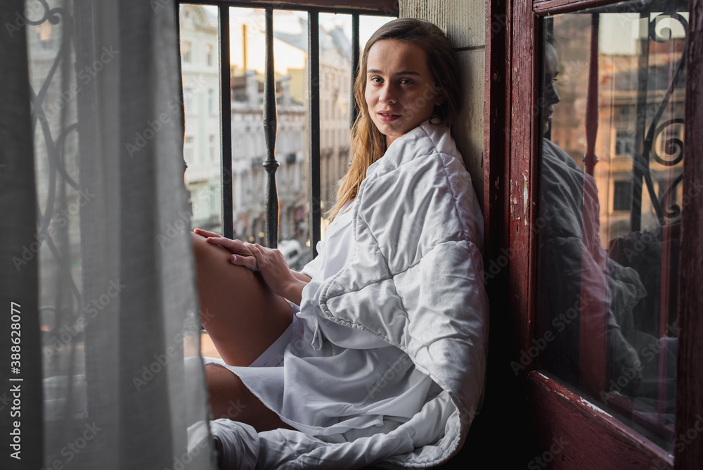 Portrait of a happy young girl. Morning sunrise girl sitting on the balcony wrapped in a bright blanket, nice morning. Selective focus