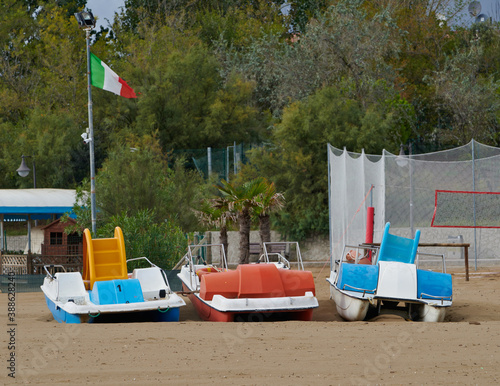 Fototapeta Naklejka Na Ścianę i Meble -  Three paddle boats with Italian flag on a empty beach in Caorle, Venice, Italy, at the end of the summer season.