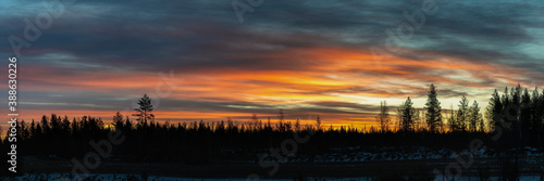 Panorama on spectacular extremely red orange colored sunrise over the Scandinavian pine tree forest, totally calm weather, forest silhouette on horizon line, frosty winter morning. Northern Sweden