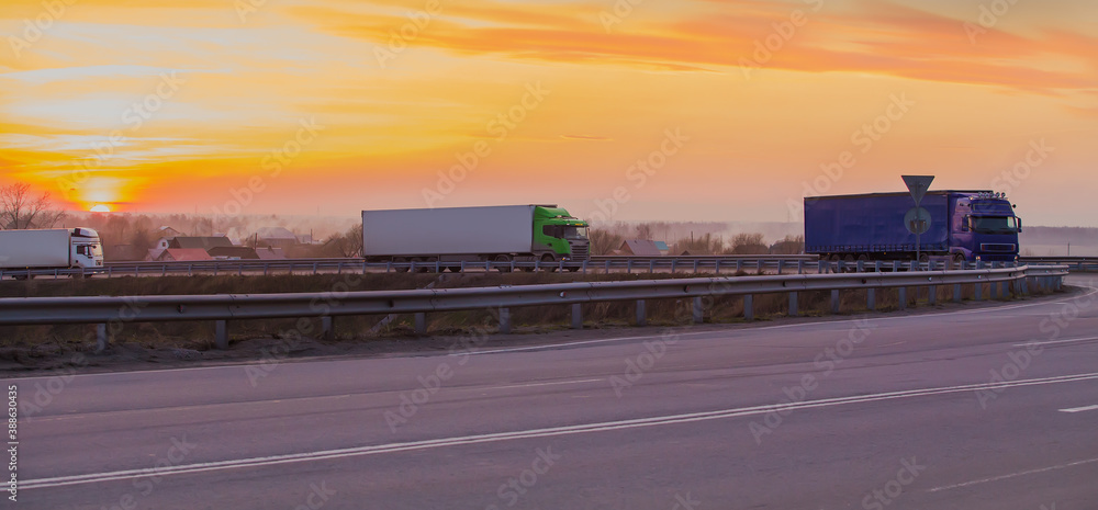 Trucks move at sunset on a suburban highway at a road junction