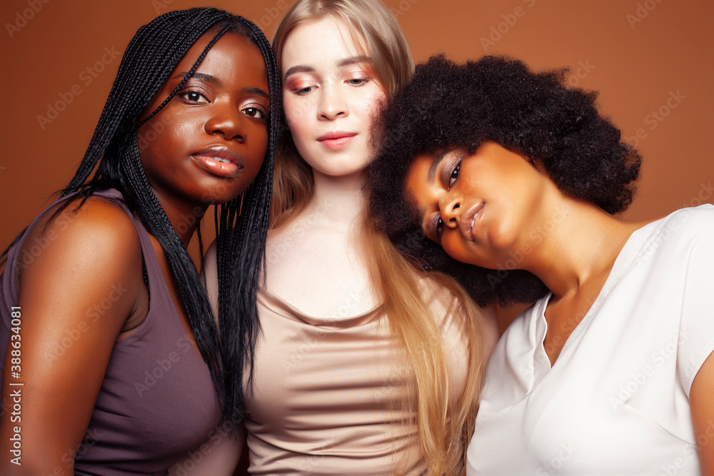 Obraz premium young pretty caucasian, afro, scandinavian woman posing cheerful together on brown background, lifestyle diverse nationality people concept