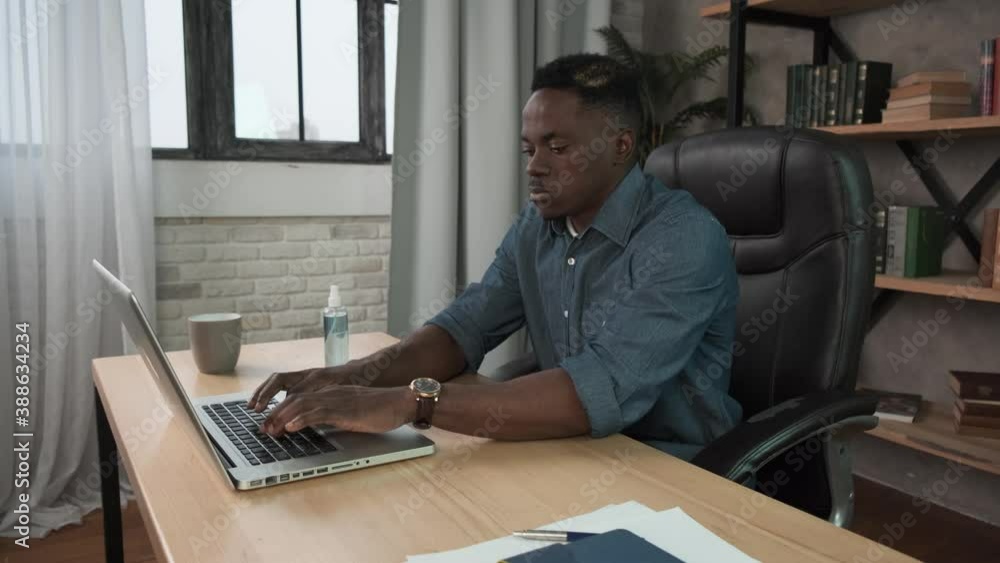African american man applying sanitizer spray rubbing hands before distance computer work from home office on remote quarantine. Male worker wearing mask using sanitiser. Corona virus protection African american man applying sanitizer spray rubbing hands before distance computer work from home office on remote quarantine. Male worker wearing mask using sanitiser. Corona virus protection