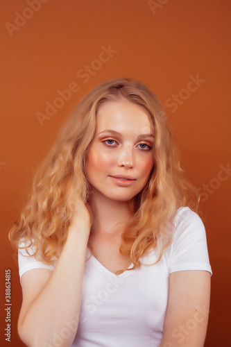 young pretty girl with blond curly hair posing cheerful on brown background, lifestyle people concept