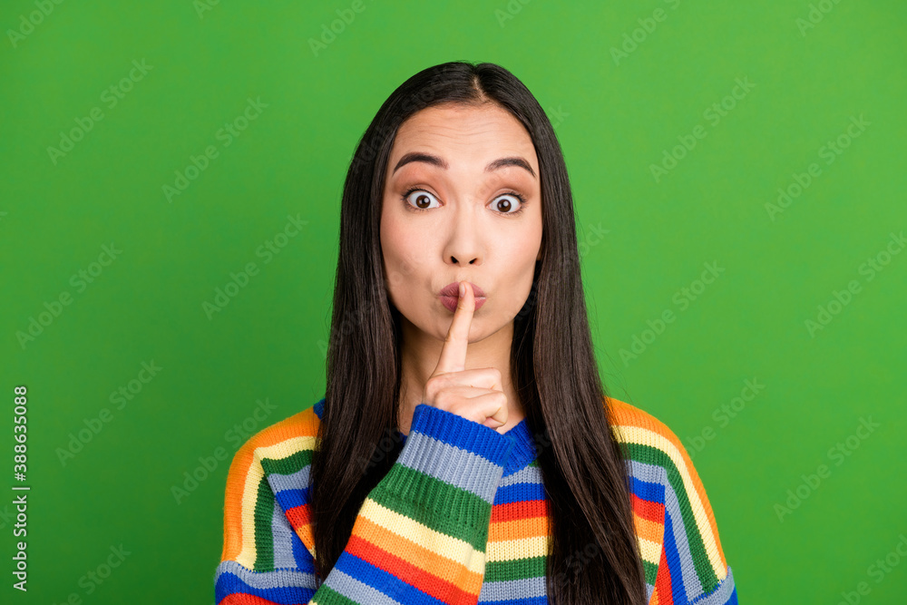 Close-up portrait of attractive mysterious girl showing shh sign keep silence isolated over bright green color background Close-up portrait of attractive mysterious girl showing shh sign keep silence isolated over bright green color background