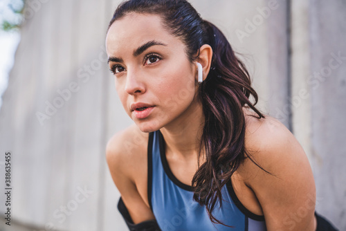 Close up shot of young pretty caucasian female athlete resting after jogging with earbuds against grey wall photo