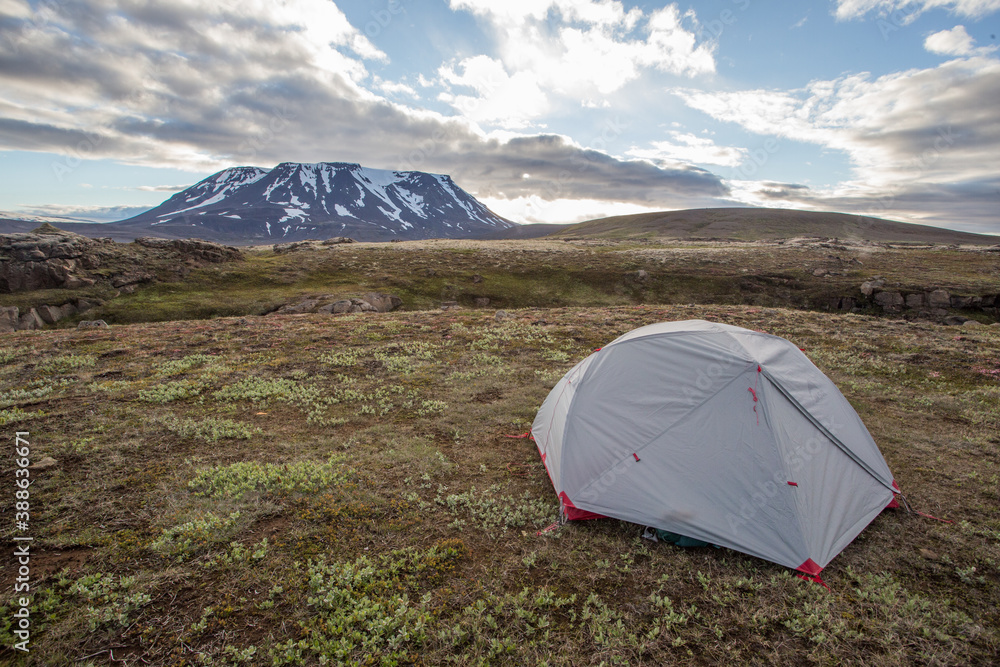 Tent in Icelandic nature with snow covered hill and blue sky with clouds. Concept of adventure on travels in Scandinavian nature. Wide angle of camping in wilderness with copy space.