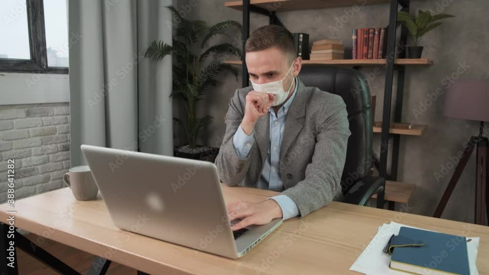Young businessman coughs into protective face mask working in the office. Caucasian man with acute viral infection while working remotely from home. Work during self-isolation and quarantine COVID-19 Young businessman coughs into protective face mask working in the office. Caucasian man with acute viral infection while working remotely from home. Work during self-isolation and quarantine COVID-19