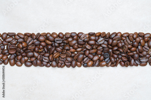 Brown coffee beans on background of light texture recycled eco-friendly paper. Central horizontal location objects, copy space for text at top and bottom. Flat lay, close-up view of still life.
