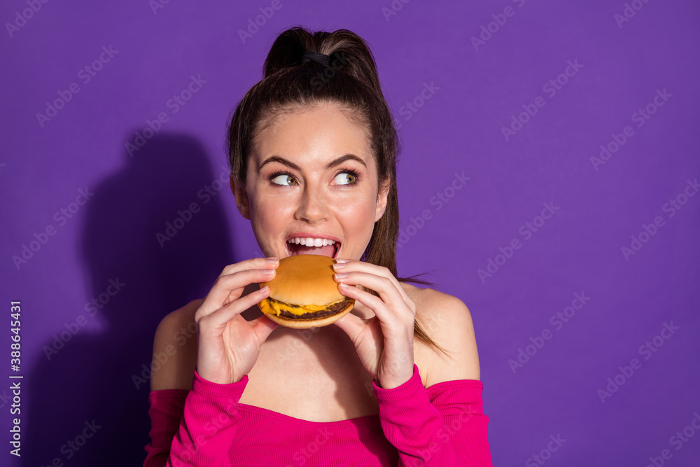 Close-up portrait of attractive cheerful girl eating fresh hot burger thinking copy space isolated on bright violet color background