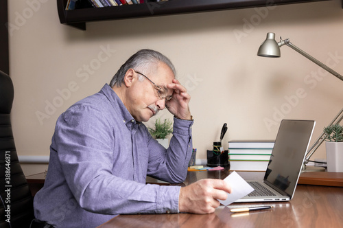 Senior man learn to use computer. Old man in glass and blue shirt Reads instructions for work using a laptop computer for online studying at home office