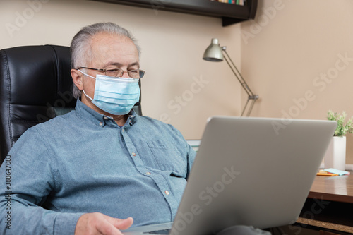 senior man in face mask working or communicate on laptop at home. study, training, work, communication, entertainment, leisure during the coronavirus period.