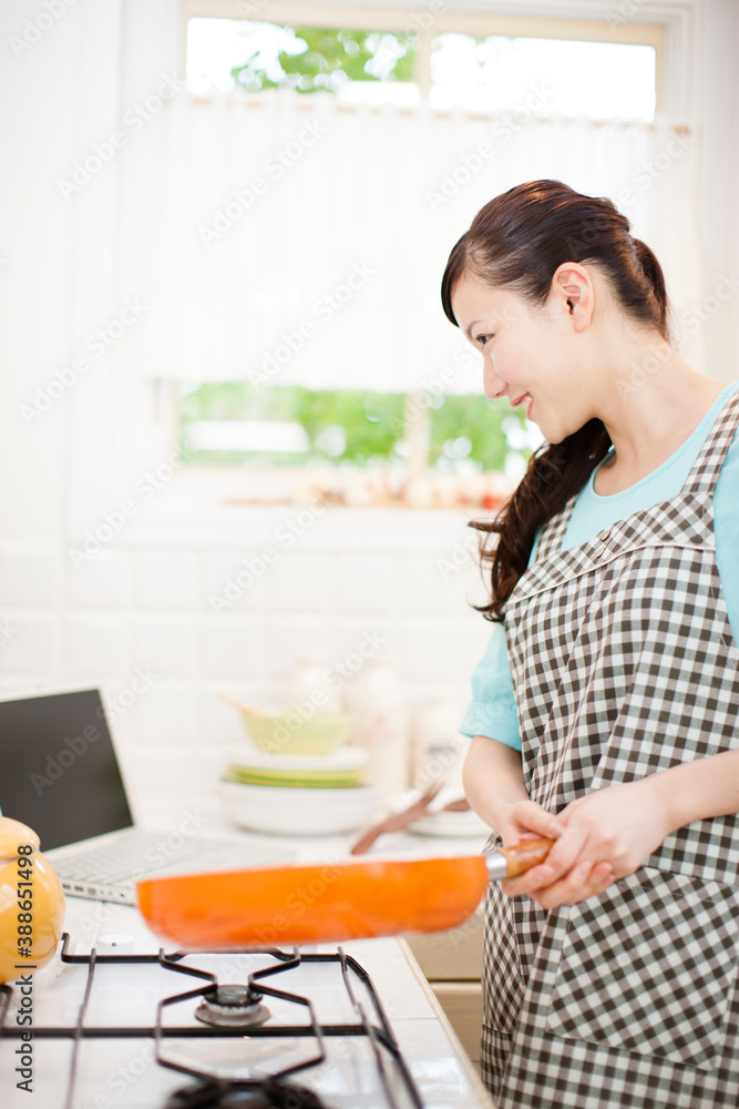 パソコンを見ながら料理する女性