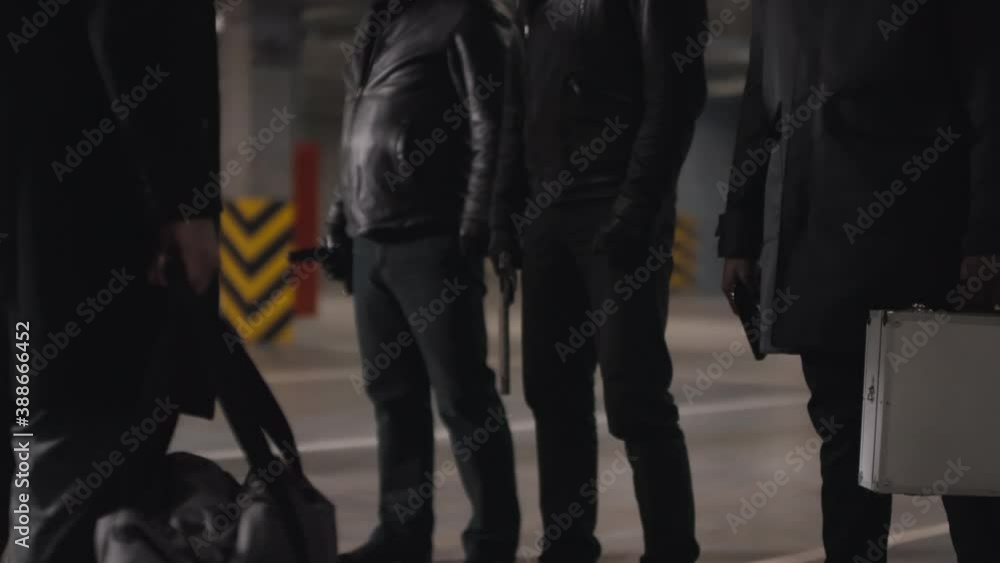 Sequence of shots of assertive multi-ethnic bandits meeting at dark underground parking transmitting briefcase with money Sequence of shots of assertive multi-ethnic bandits meeting at dark underground parking transmitting briefcase with money