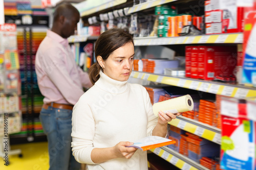 Young woman customer choosing different office supplies in stationery shop