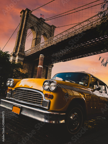 Fototapeta Vintage yellow taxi cab in New York under the Brooklyn Bridge with a colorful sk