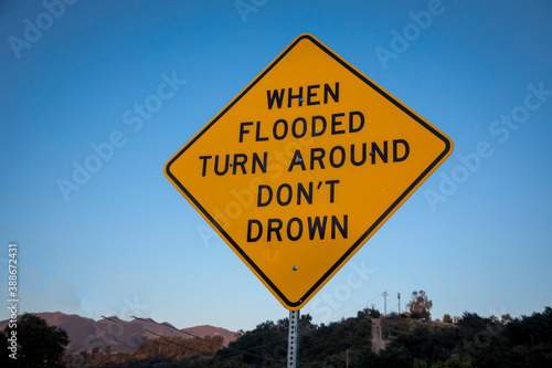 A yellow and black diamond shaped traffic sign warning about drowning in a flood.