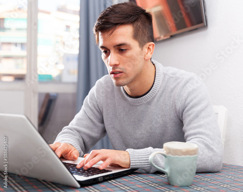 Portrait of cheerful male who is working with laptop at the table at the home