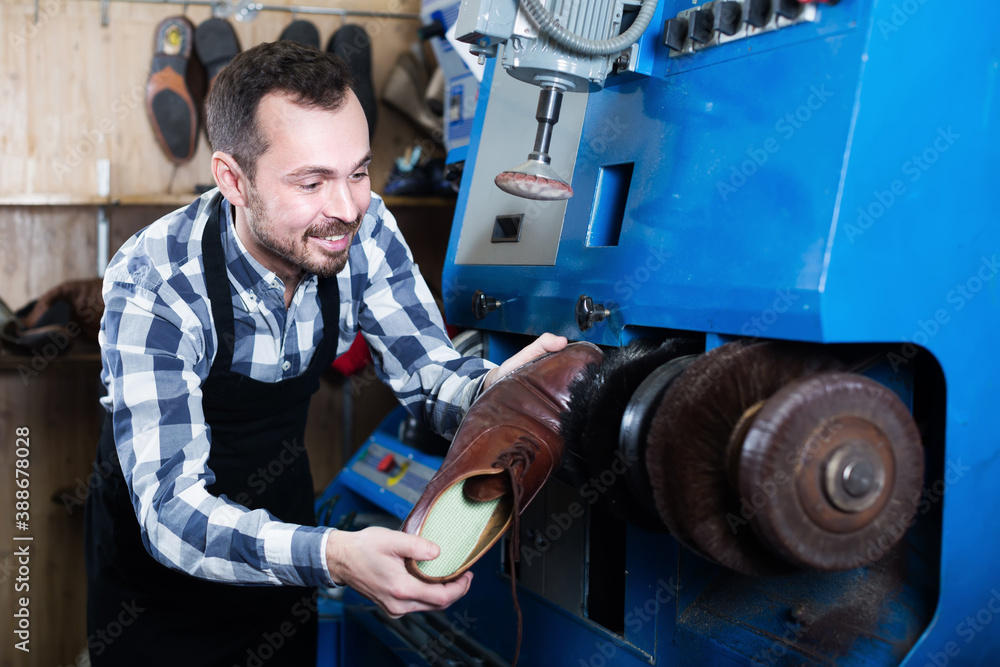 Young male worker working at restoring boot in repair workshop