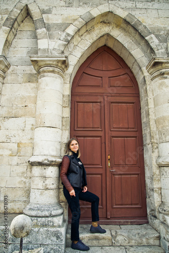 young woman in a leather jacket near the entrance to the ancient wooden door of a gothic temple © Виктория Бычкова