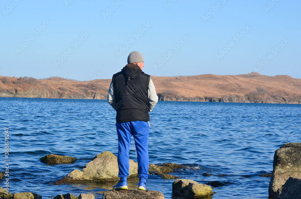 a man stands on a rock on the beach in the autumn and breathes fresh air, healthy lifestyle and sports style