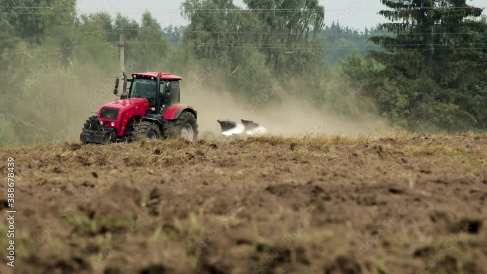 Red tractor plows dusty farmland with skidding. Agricultural machine does not efficiently process arable land with compaction of the soil under the wheels. Seasonal field work in Sunny weather Red tractor plows dusty farmland with skidding. Agricultural machine does not efficiently process arable land with compaction of the soil under the wheels. Seasonal field work in Sunny weather