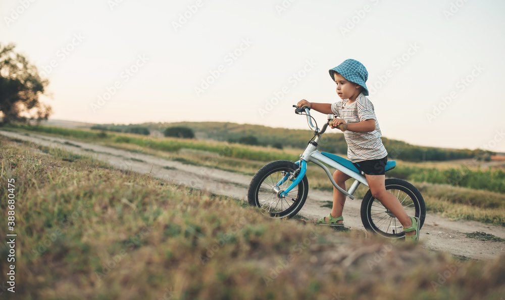 Side view photo of a caucasian boy with blue hat riding a bike on a country road