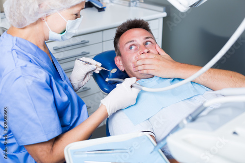 Young man frightened by dentist covering her mouth