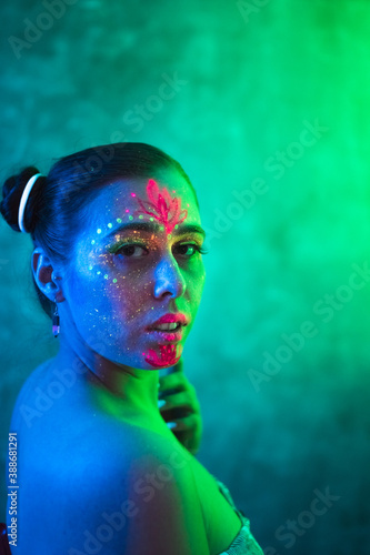 Portrait of beautiful naked woman with ethnic pattern, neon makeup in colorful lightings. Fluorescent paints in ultraviolet light.