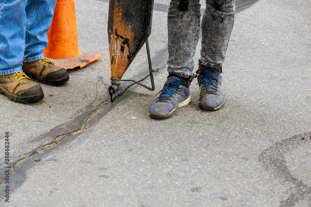 Workers perform minor repairs to pavement by spraying liquid asphalt into pits on roadway sealing cracks road construction Workers perform minor repairs to pavement by spraying liquid asphalt into pits on roadway sealing cracks road construction